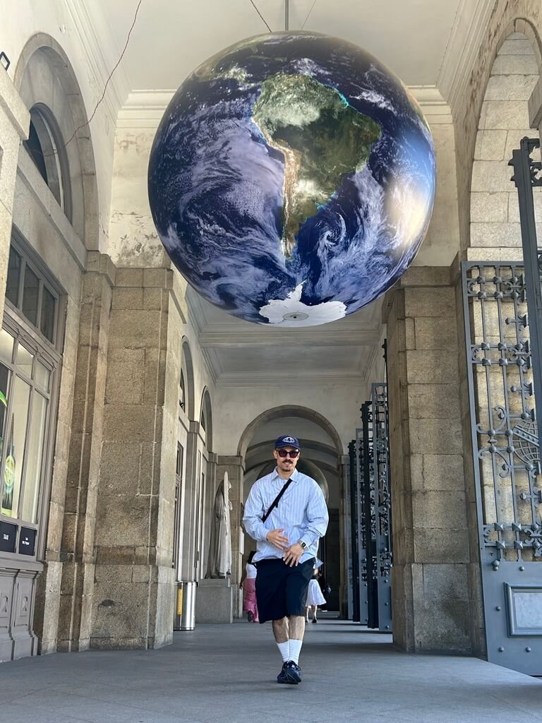 A dancer walking beneath a large suspended globe in an indoor hall — Porto 2025.